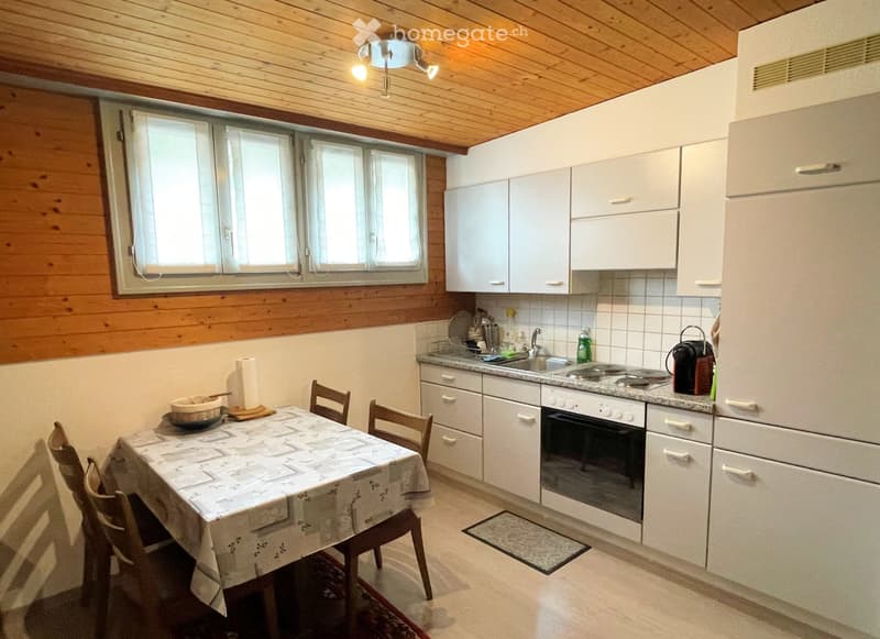 Bright kitchen with white cabinets, a dining table with chairs, and a window letting in natural light. The kitchen features a sink, stove, and refrigerator.