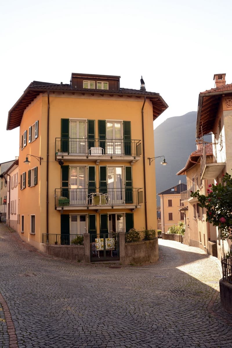 Two-story yellow building with green shutters, balconies, and a cobblestone street in front.