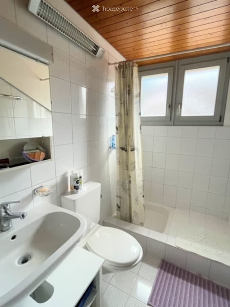 Modern bathroom with white tiles, wooden ceiling, sink, toilet, bathtub, and shower curtain.