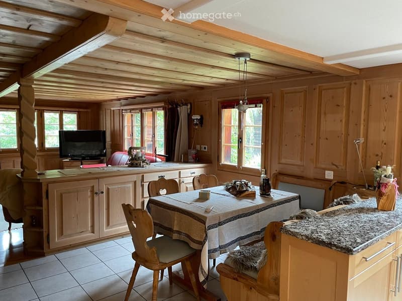 A cozy, wooden-paneled room with a dining table, chairs, a television, and a kitchen area with cabinets and a countertop.