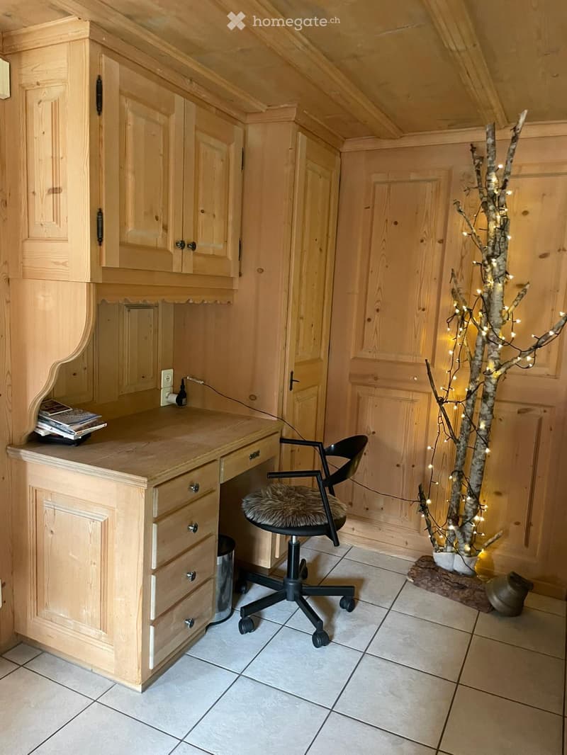 A cozy, wooden-paneled room with a large wooden desk, a black office chair with a fur seat, built-in cabinets, and a decorative tree with lights.