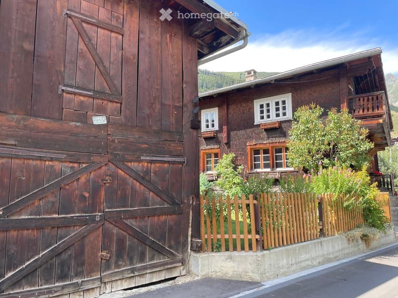 Traditional wooden house with a wooden gate, white-framed windows, and a wooden fence in front.