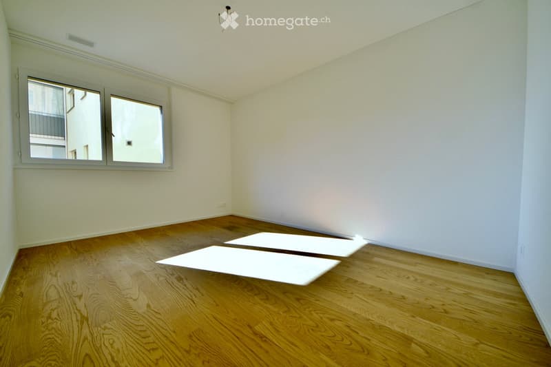 Empty room with wooden flooring and white walls, featuring two large windows with white frames and a visible balcony outside one window.