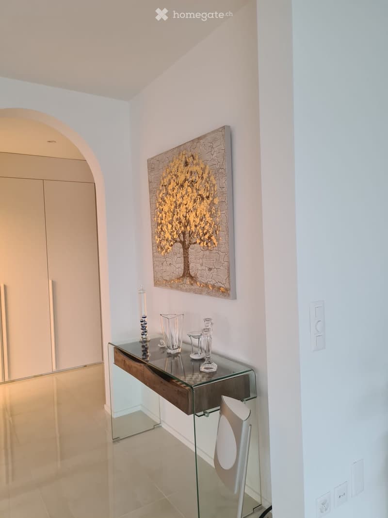 Modern hallway with a glass console table, decorative items, and a large abstract painting on the wall.
