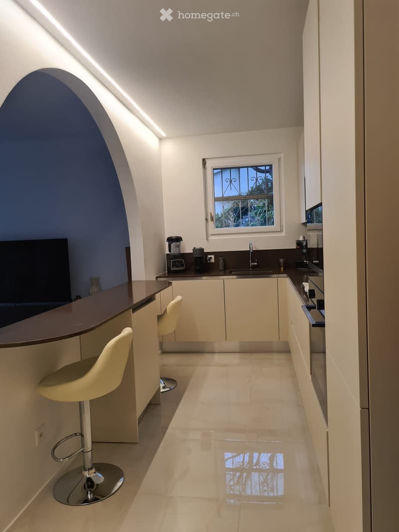 Modern kitchen with white cabinets, dark countertops, a window, and two yellow stools at the island.
