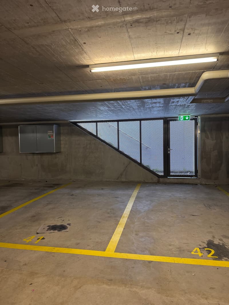 concrete floor, yellow parking lines, grey cabinet, emergency exit door, white lighting fixture