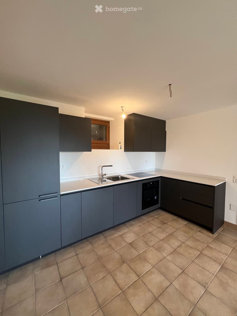 Modern kitchen with dark grey cabinets, a sink, and an oven. The floor is tiled in a warm beige color.