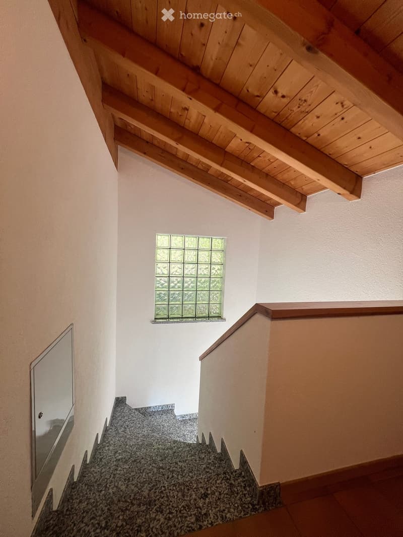 Staircase with wooden handrail and a small window with decorative glass panes above the stairs.