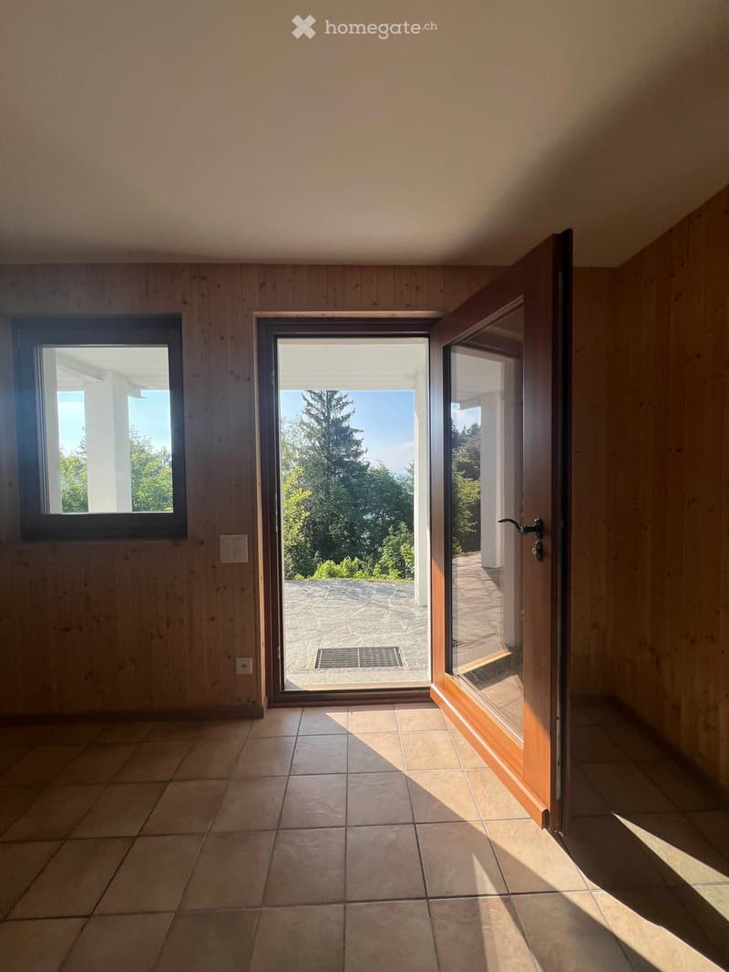Empty room with wooden walls, tiled floor, and large sliding glass door leading to an outdoor area with a view of trees and a stone patio.