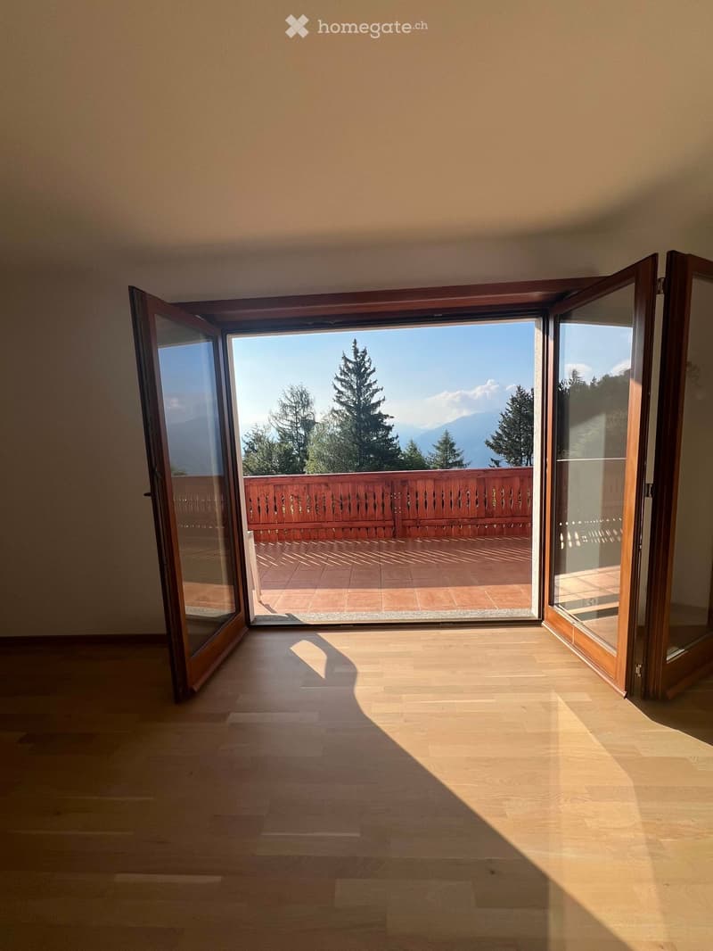 Empty room with wooden flooring and large open sliding doors leading to a balcony with a scenic mountain view.