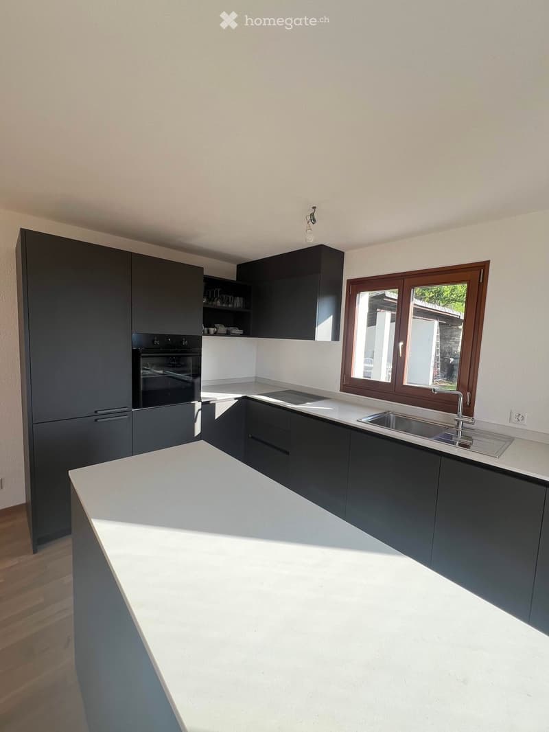 Modern kitchen with dark grey cabinets, white countertops, and a large island. Features an oven, sink, and ample storage space.