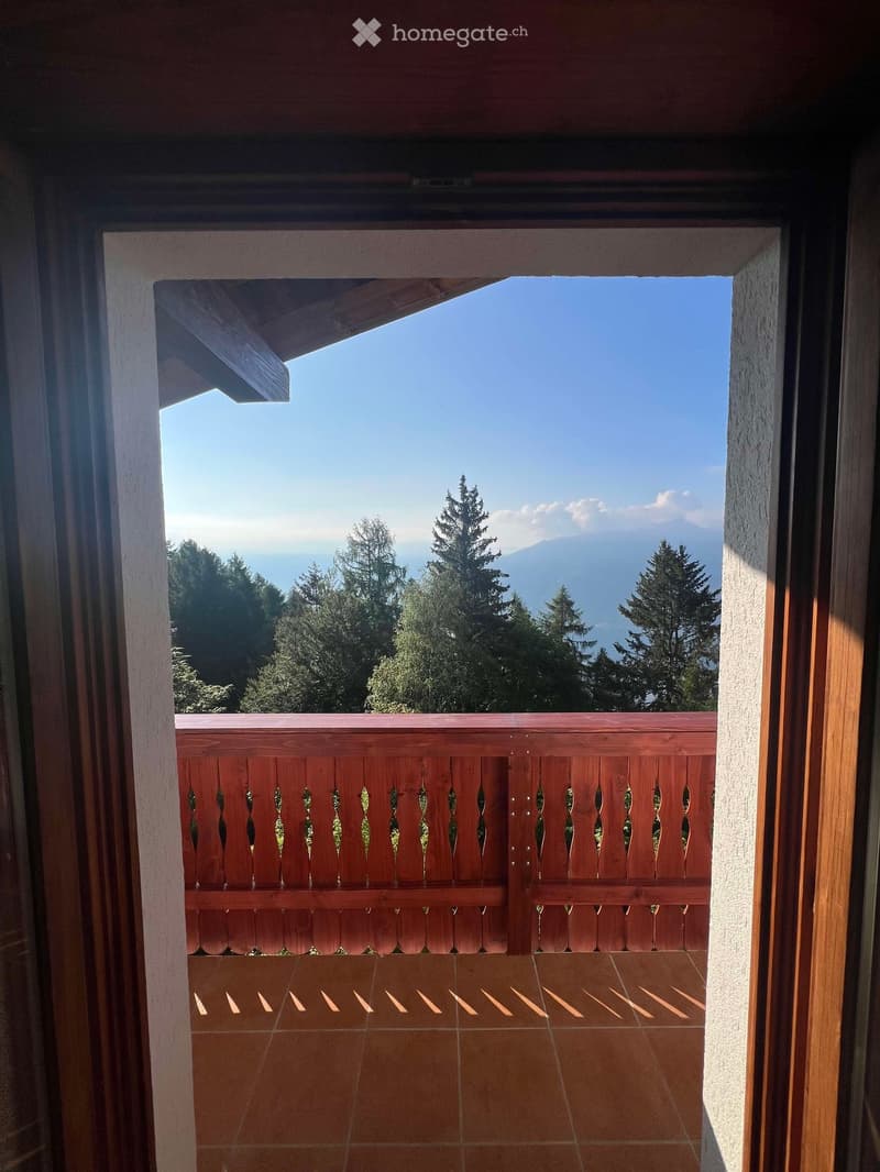 Balcony with wooden railing and tiled floor, overlooking a scenic view of trees and mountains.
