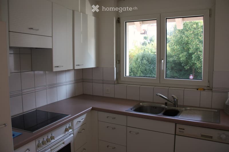 Modern kitchen with white cabinets, a stainless steel sink, a built-in oven, and a dishwasher. The countertops are light brown, and the backsplash is tiled.