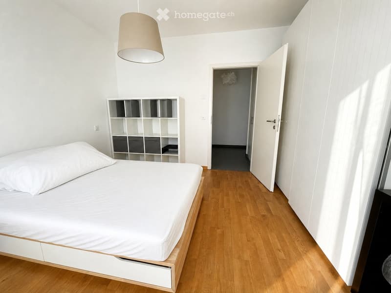 Minimalist bedroom with a single bed, white bedding, a modern shelf unit, and wooden flooring.