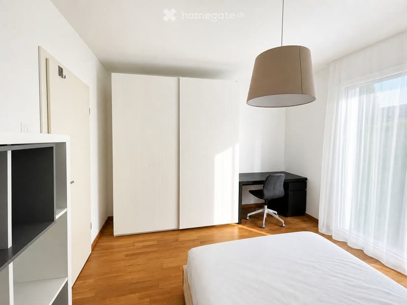 Modern bedroom with a white bed, a black desk with a chair, a large white wardrobe, and a pendant light hanging from the ceiling.