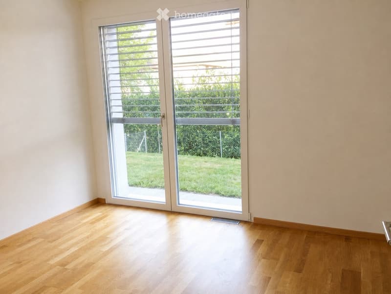 Empty room with wooden flooring and large sliding glass doors leading to a green outdoor area.