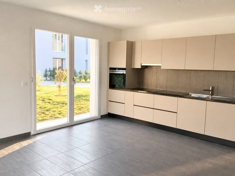 Modern kitchen with light-colored cabinets, a stainless steel sink, and an oven. The space features large windows and a tiled floor.