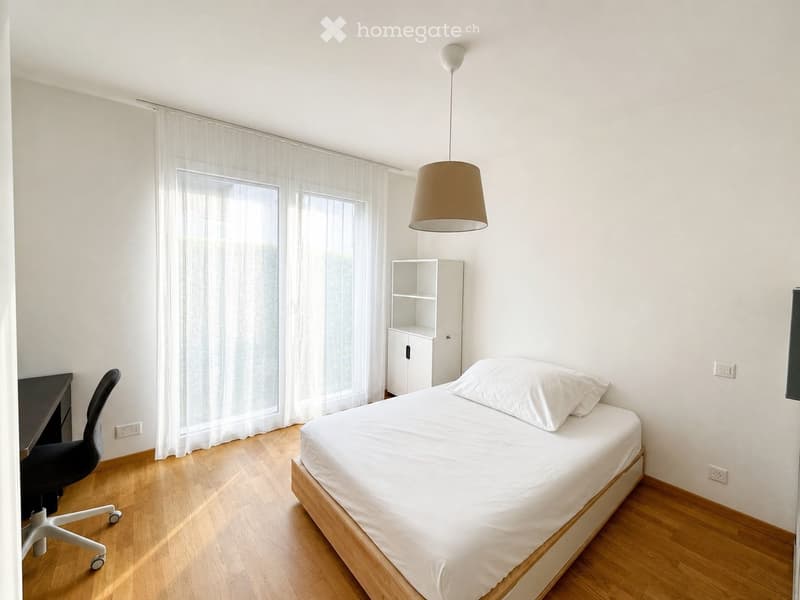 Minimalist bedroom with a single bed, white bedding, a small desk with a chair, a white cabinet, and a pendant light fixture.