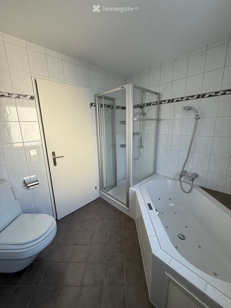 The bathroom features tiled floors, a white bathtub with jacuzzi jets, a separate shower with a glass door, a white toilet, and white tiled walls.