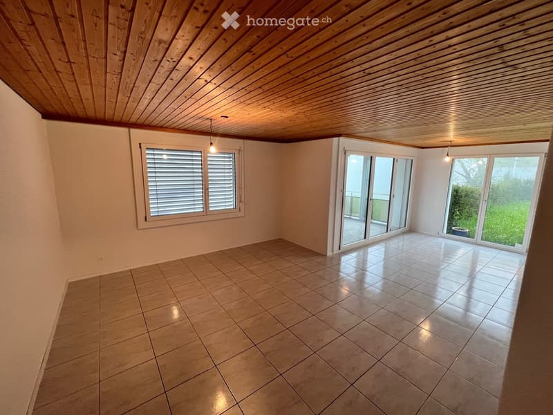 Empty room with wooden ceiling, tiled floor, large windows, and sliding glass doors leading to a balcony.