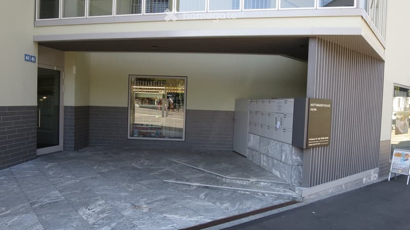 Entrance area of a building with a raised ground floor, featuring a tiled floor, mailboxes, and a sign displaying the address "HOTTINGERSTRASSE 44/46".