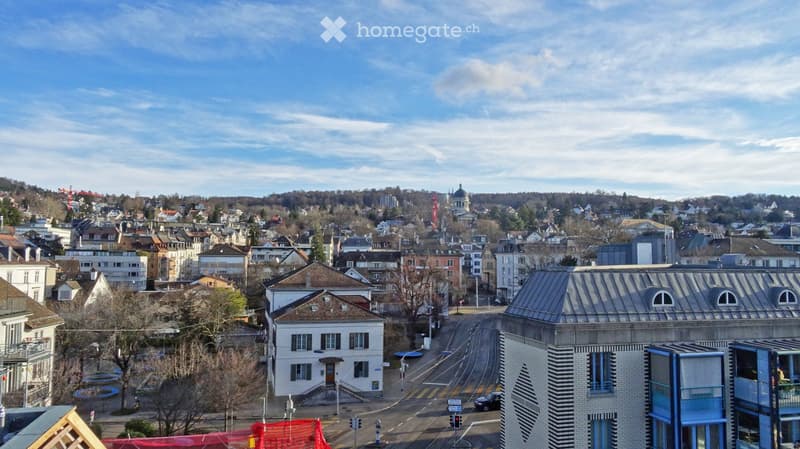 A panoramic view of a cityscape with a mix of residential and commercial buildings, a tram line, and a church dome in the distance.