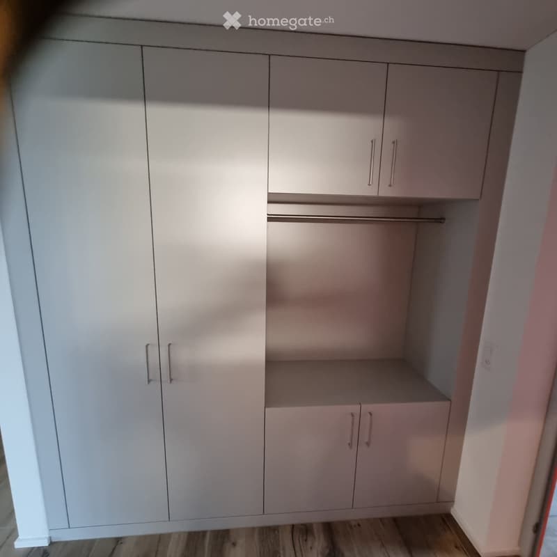 Empty closet with white built-in cabinets and a wooden floor. No furniture or items present.