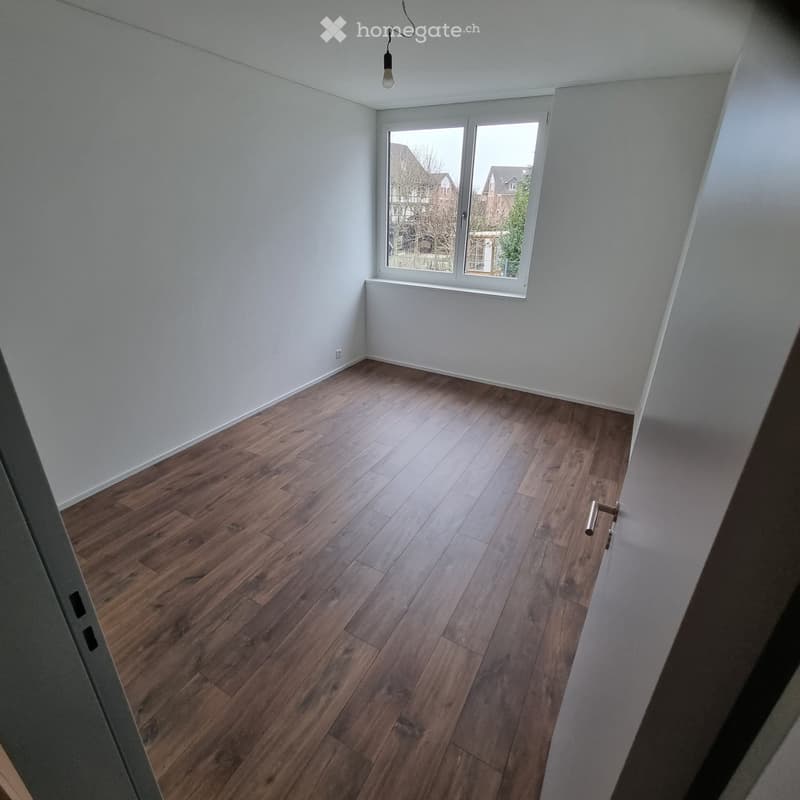 Empty room with wooden flooring, white walls, and a large window with white frame. No furniture or equipment present.