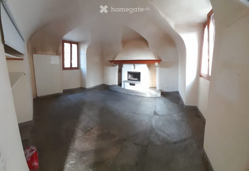 Empty room with stone floor, arched ceiling, fireplace, and two windows.