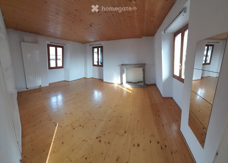 Empty room with wooden flooring, white walls, and several windows. A fireplace is present but no furniture or furnishings.