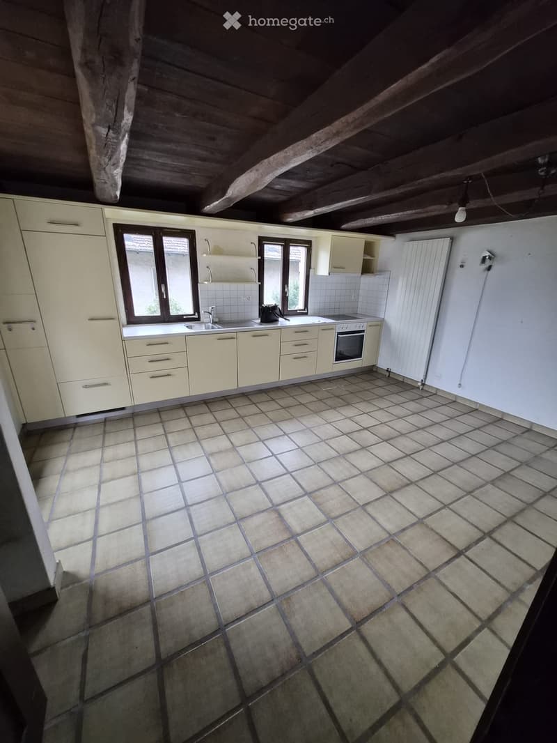 Bright kitchen with cream-colored cabinets, tiled floor, and exposed wooden beams on the ceiling. Features a sink, oven, and radiator.
