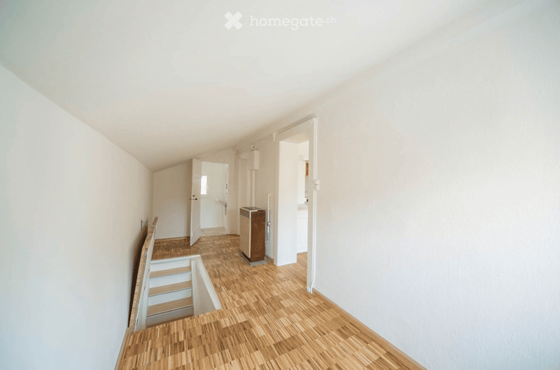 Empty hallway with wooden flooring, white walls, and open doors leading to other rooms. A small trash bin is visible near the center.