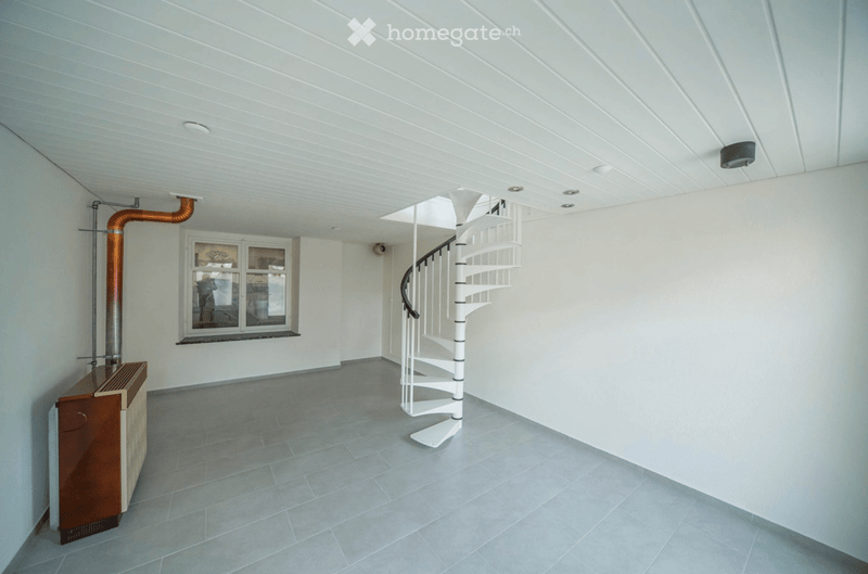Modern hallway with a white spiral staircase, grey tiled floor, white walls, and a window with a view of the outside.