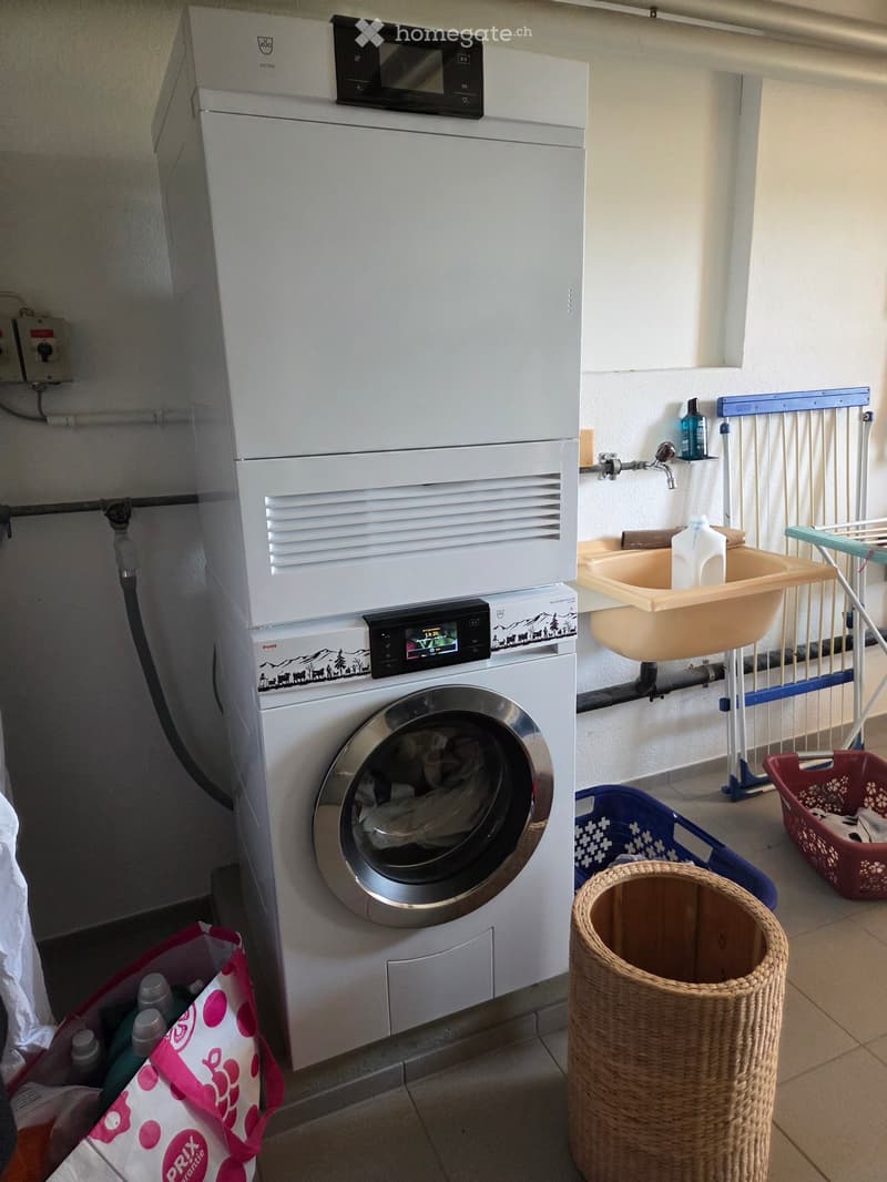 Bathroom with a washing machine, a small sink with a faucet, laundry baskets, and a wicker basket on the floor.