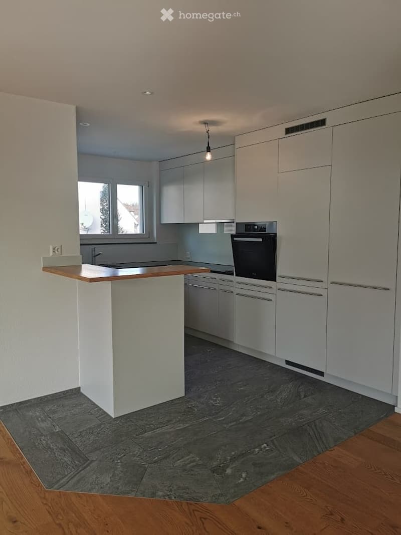 Modern kitchen with white cabinetry, a built-in oven, a central island with a wooden countertop, and a sleek, dark tiled floor area.