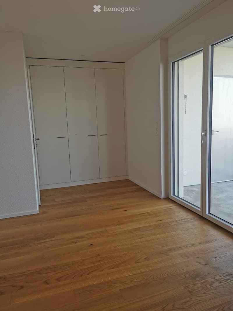 Empty room with wooden flooring, white walls, built-in closet, and large sliding glass door leading to a balcony.