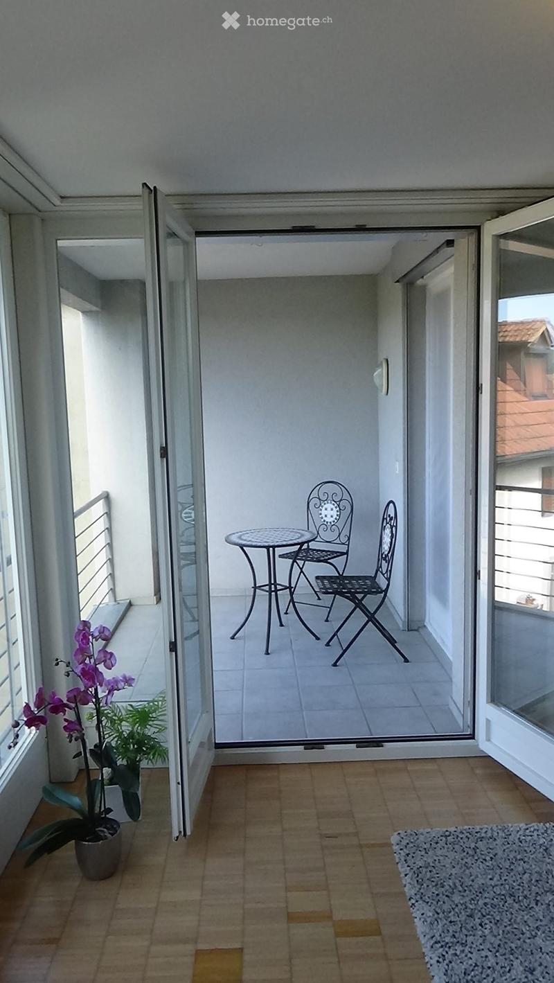 Balcony with a small round table and two chairs, potted orchid, and sliding glass doors leading to the interior.