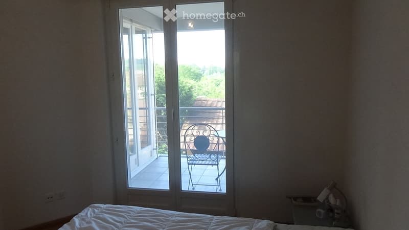 Bedroom with a bed, nightstand, and lamp, featuring large sliding glass doors opening to a balcony with a decorative metal chair.
