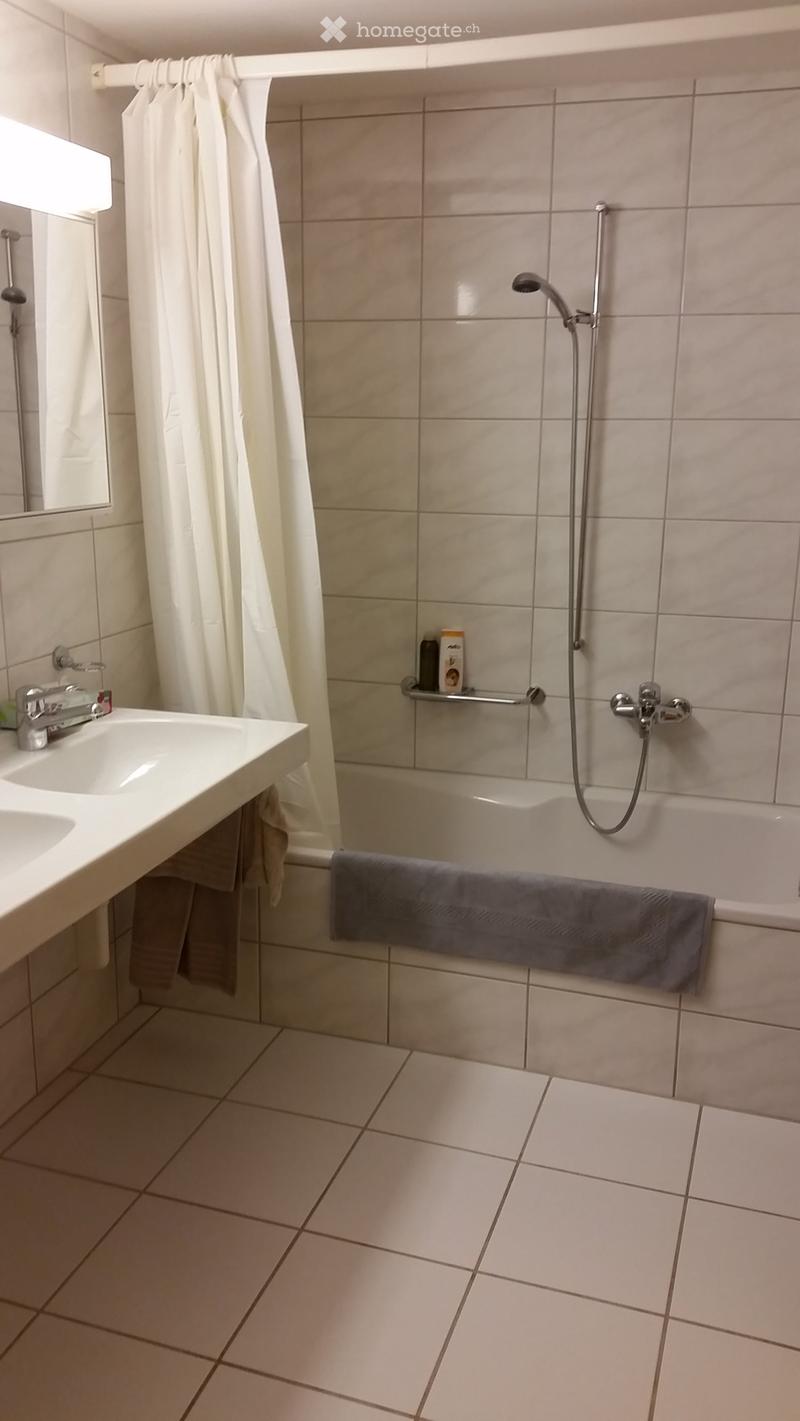 Modern bathroom with beige tiles, a white sink, a bathtub with a shower, and a towel on the edge.