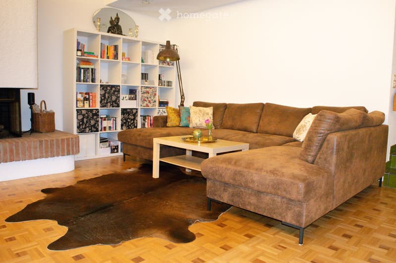 Modern living room with a brown sectional sofa, coffee table, bookshelf, floor lamp, and fireplace.