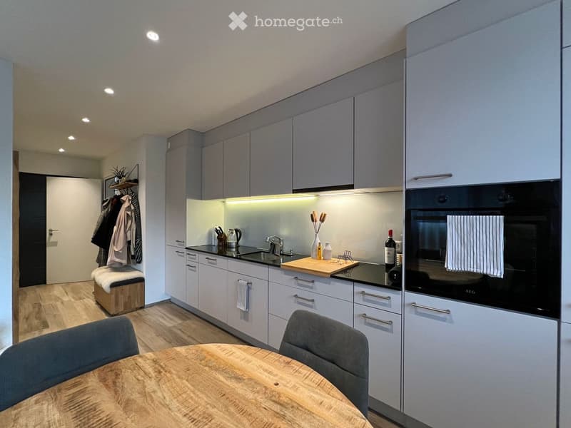 Modern kitchen with light grey cabinets, black countertops, a wooden dining table, and a bench in the corner.