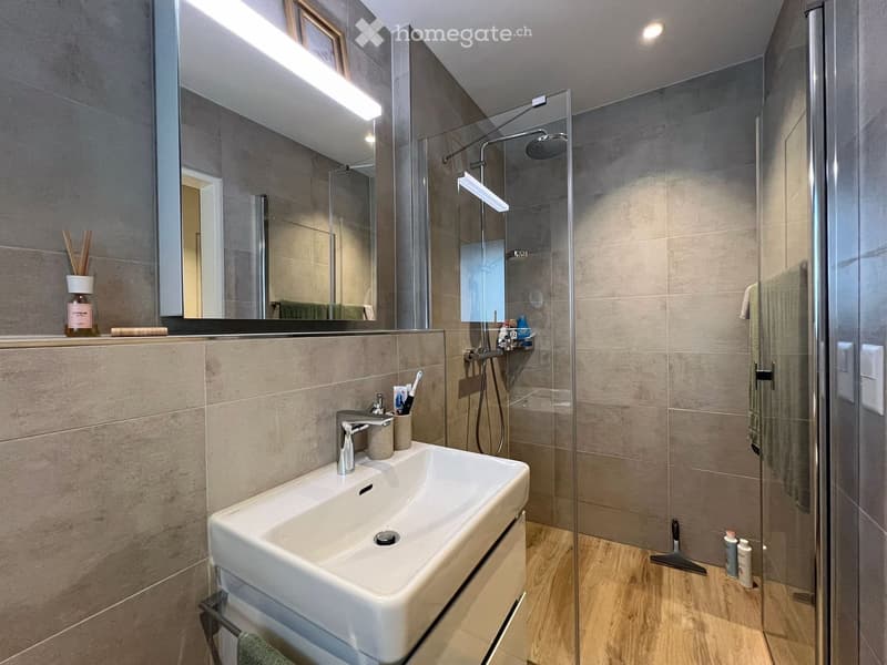 Modern bathroom with a white sink, chrome faucet, large mirror, glass-enclosed shower, and wooden floor.