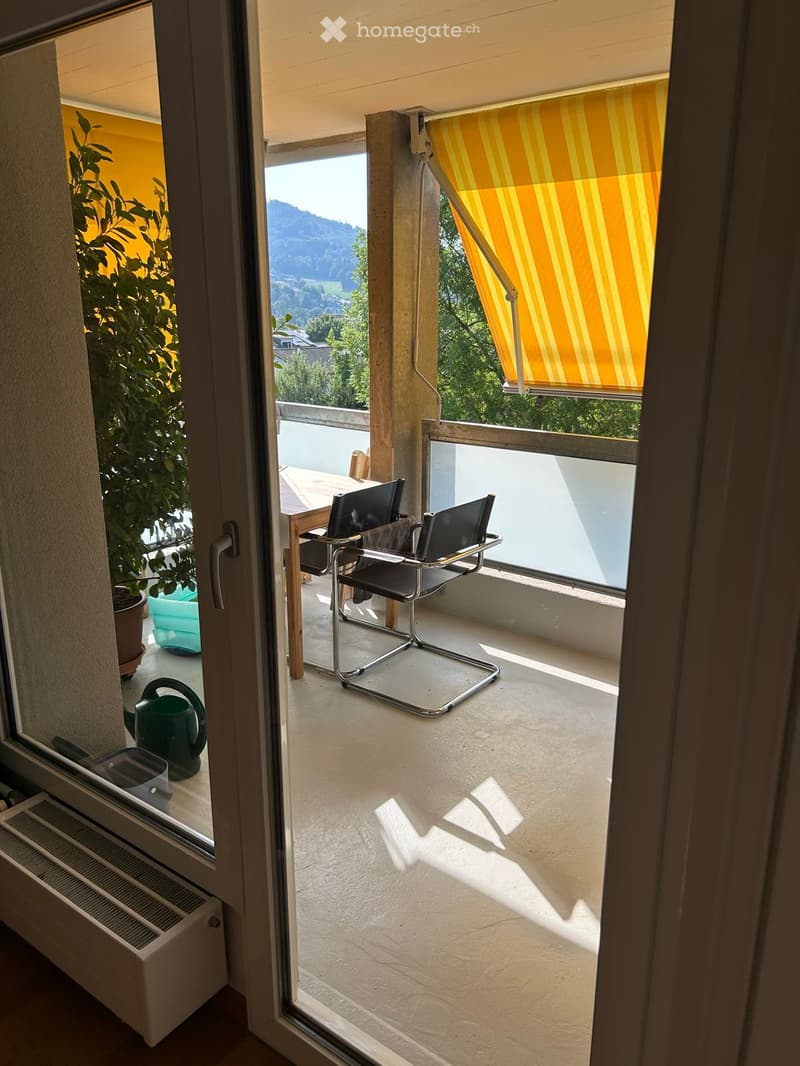 Balcony with a view, featuring a table and two chairs, a green watering can, and a potted plant.