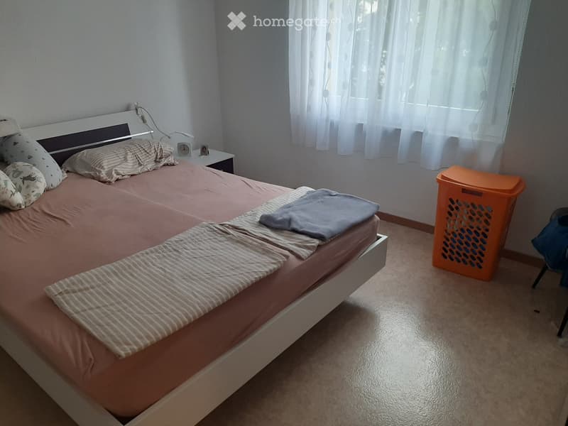 Bedroom with a single bed, nightstand, clock, and laundry basket. The bed is made with striped bedding and pillows.