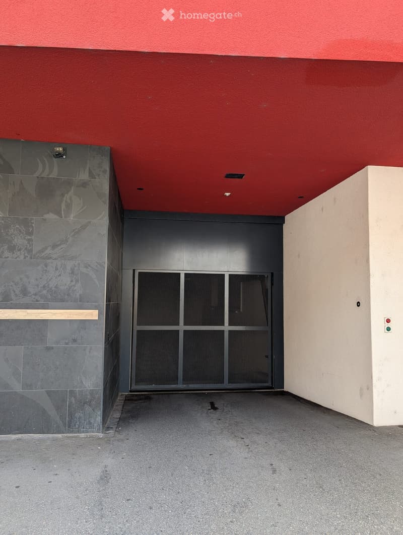 Entrance to a building with a red ceiling, grey garage door, and grey marble wall on the left.