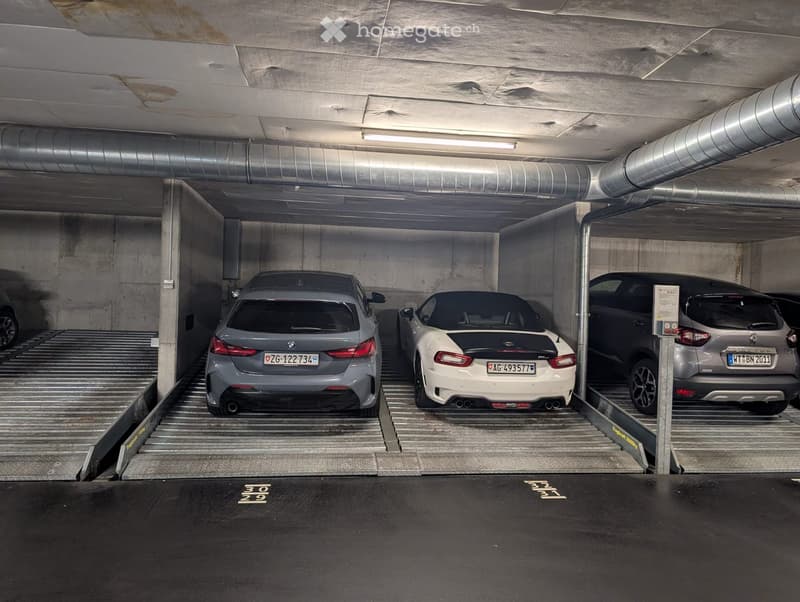 Underground parking area with several parked cars, concrete walls, and a metal staircase leading to another level.