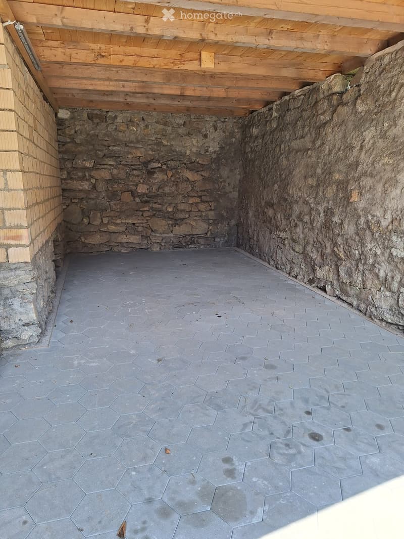 Empty space with stone walls and a hexagonal tiled floor, featuring a wooden ceiling and a small opening to the left.