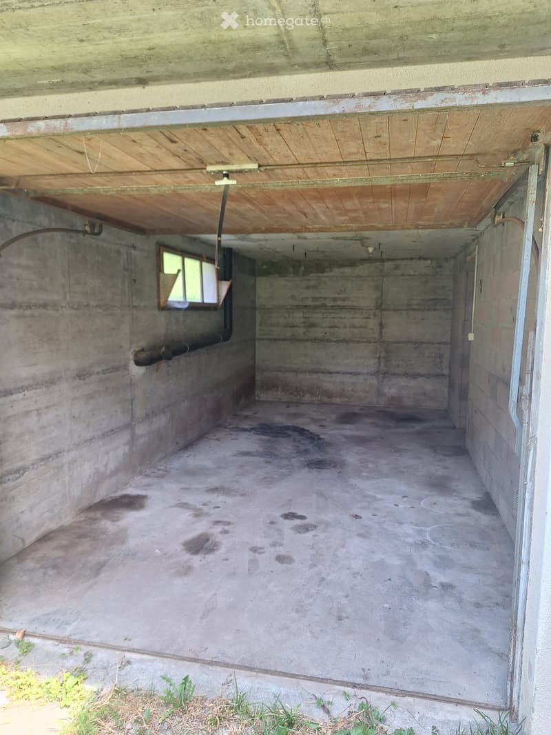 Empty concrete garage with a wooden ceiling, a small window, and a concrete floor.