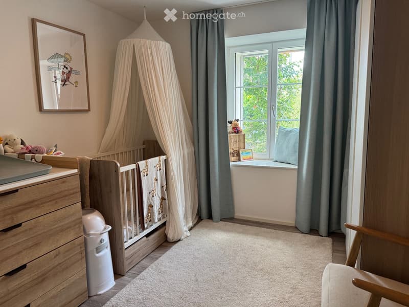 A well-lit, cozy nursery with a wooden crib, a dresser, a baby chair, a curtained crib, a picture frame, toys, a baby monitor, a baby seat, and a rug.