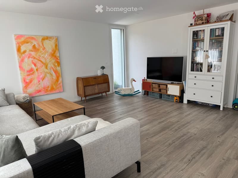 Modern living room with a grey sectional sofa, wooden coffee table, TV stand, bookshelf, and a colorful abstract painting on the wall.